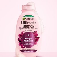 Garnier Grape Moisture shampoo bottle on a pink background